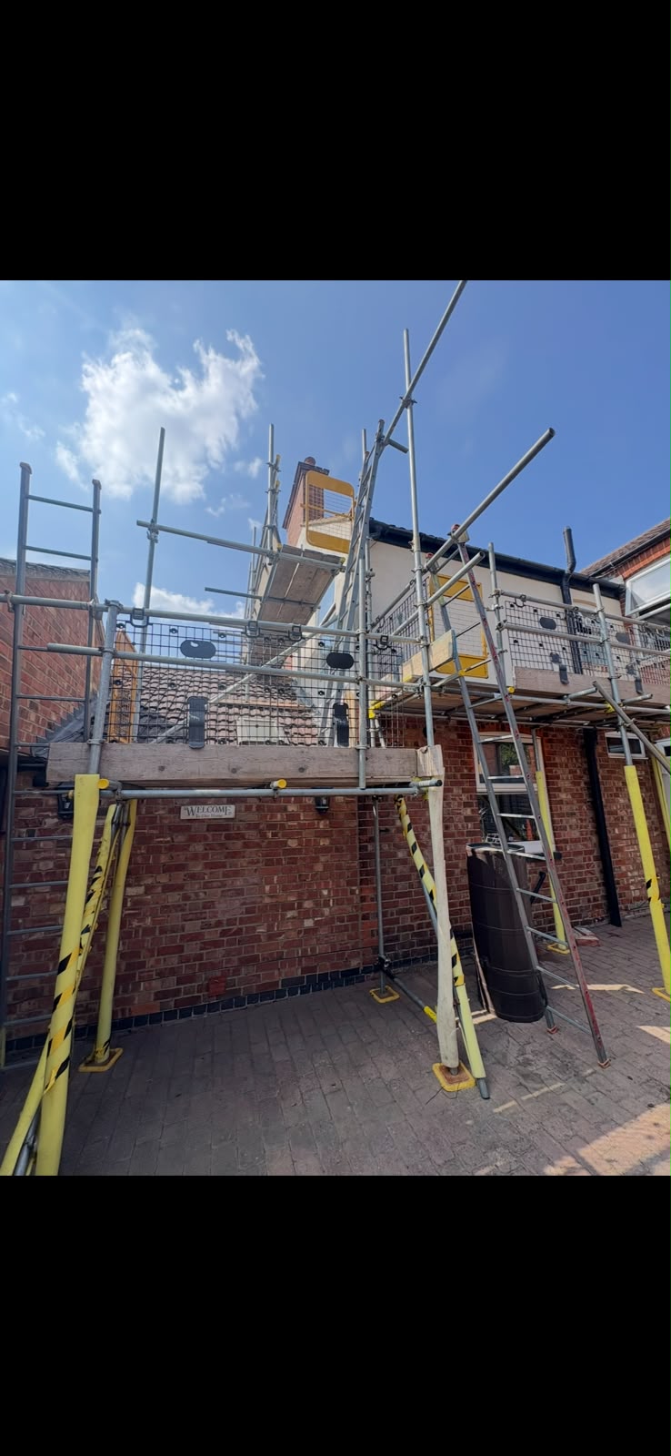 Tower scaffold with guardrails and netting to the rear of a brick property