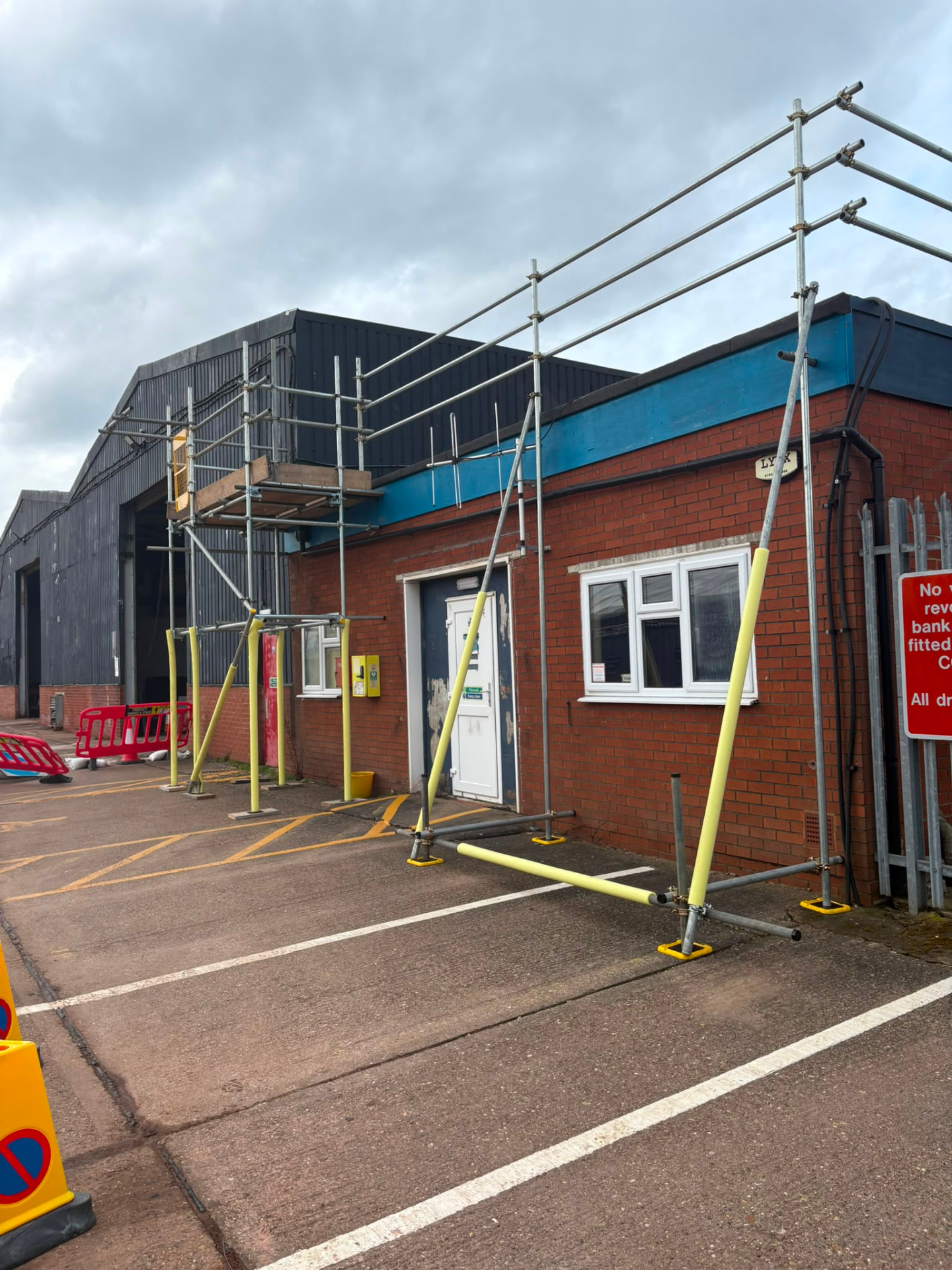 Edge protection scaffolding with padded uprights to a single storey brick unit